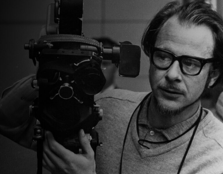 A man with glasses operates a film camera.