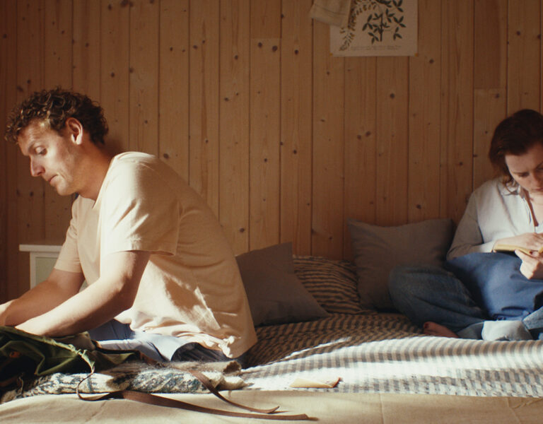 Two people sit on a bed in a wooden-panelled room. As one packs a bag and the other reads, both lost in thought, the scene echoes the quiet nostalgia of Clint Frift's "We Used to Be Fun.