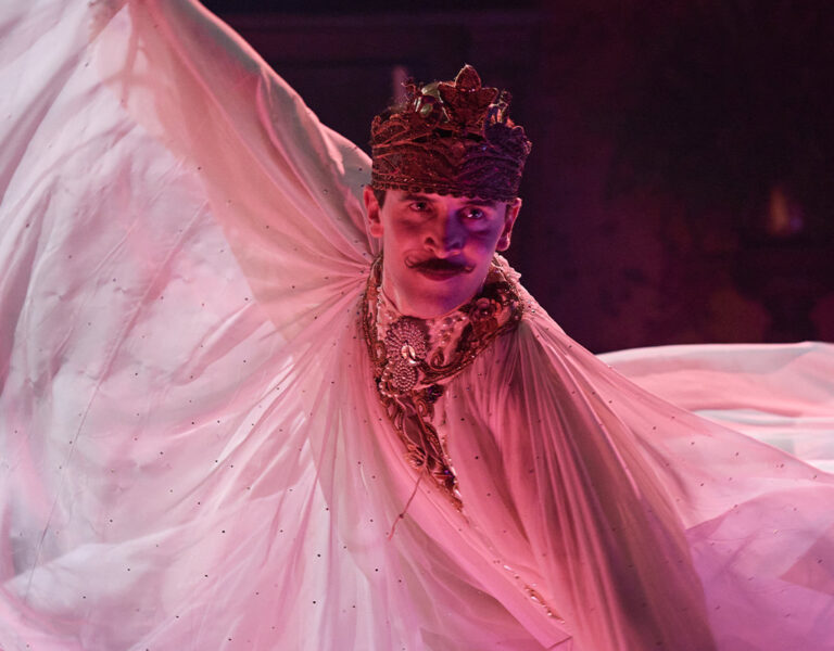 A person wearing a crown, ornate jewellery, and a dramatic flowing costume poses with arms extended amidst pink and purple lighting, capturing the vibrant energy of the BFI Flare 2026 festival programme.